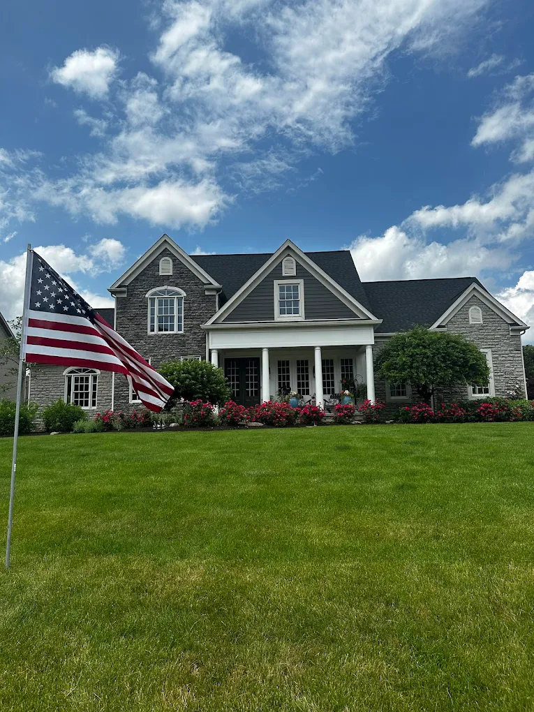 A finished two-storey home with stone facing, dark shingle roof and new gutters